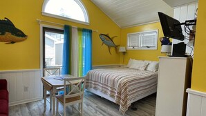 Ein Zimmer mit einem Bett, einem Schreibtisch, einem Sessel, einem Wandbild mit Fischen, einem Fenster mit Vorhängen und einem Deckenventilator.