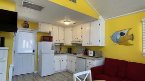 Eine kompakte Küche mit weißen Schränken, einem Kühlschrank, einer Mikrowelle und einem Toaster. Im Wohnbereich befindet sich ein rotes Sofa und ein Holztisch.