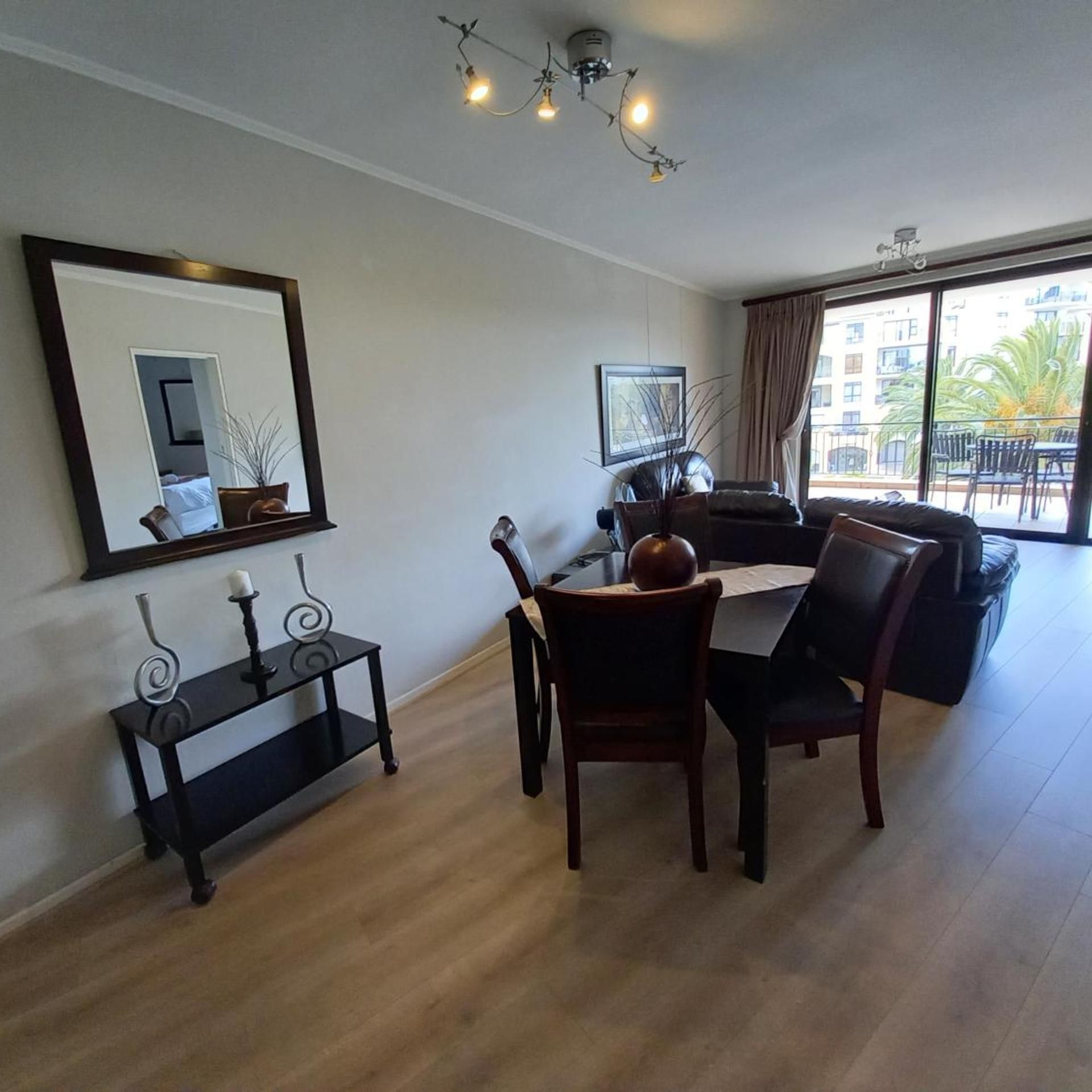 A modern living room with a dining area, a large window with a view, and a ceiling light fixture.
