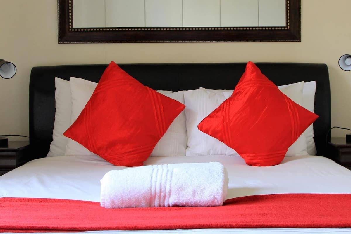 A bed with white bedding and two red pillows, a white towel, and a red blanket.
