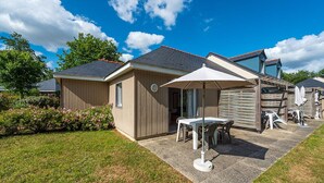 A small, single-story building with a patio area featuring a table and chairs, surrounded by a grassy lawn and a wooden fence. - Spacious Duplex Cottage in Saumur (Saumur)