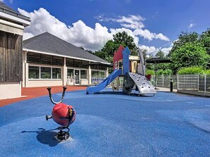 A playground with a slide and climbing structures, a building with large windows, and a red and black object on the ground. - Holiday Home With Patio in Saumur (Saumur)