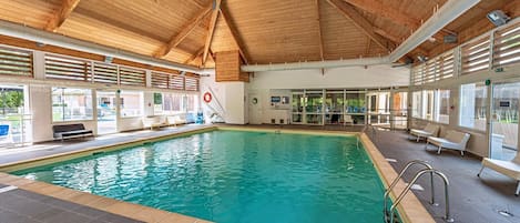 Une piscine intérieure dotée d’un plafond en bois, d’un sol carrelé et d’espaces aménagés pour s’asseoir.