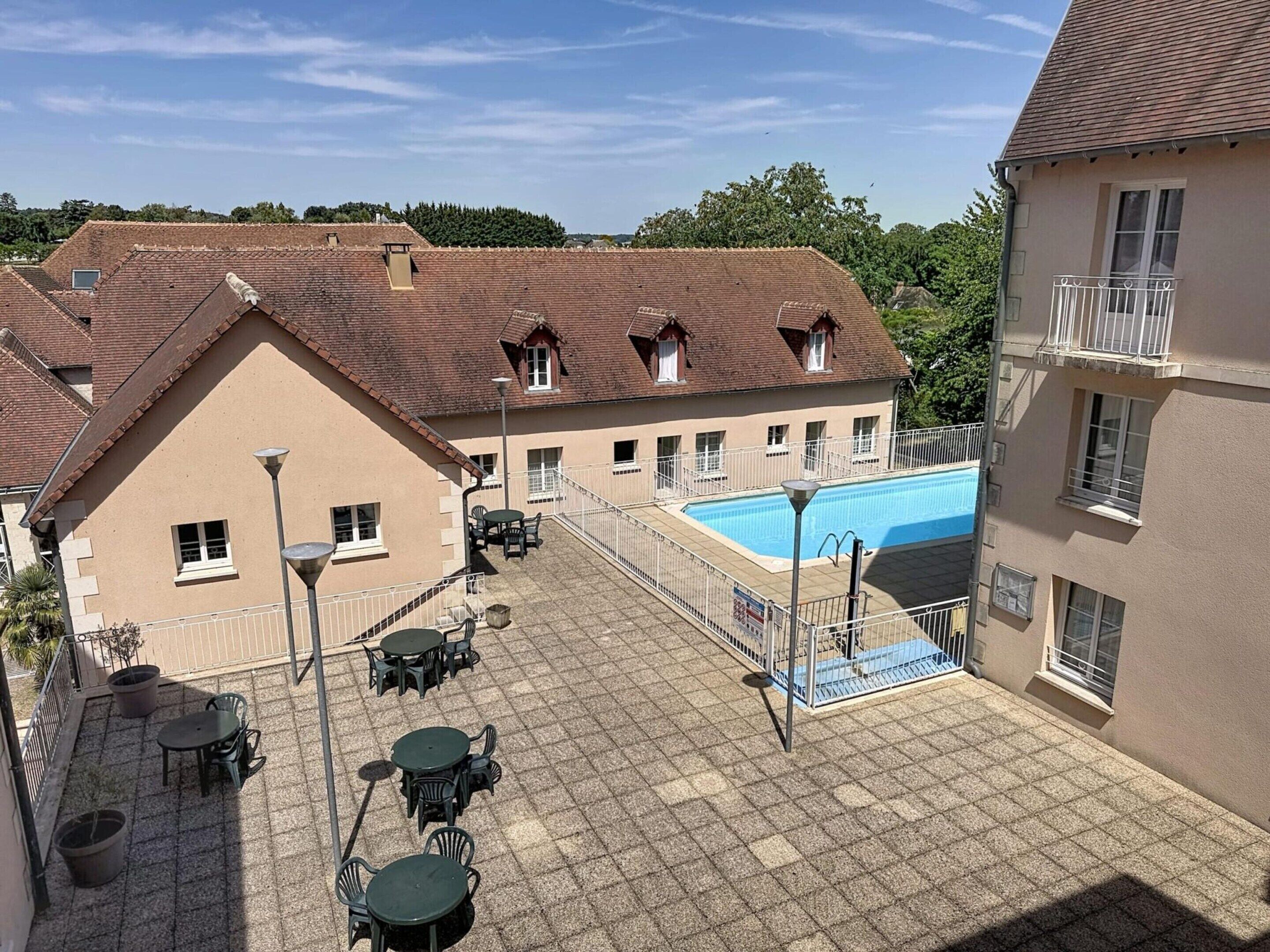 A courtyard with a swimming pool, outdoor seating, and a building with a tiled roof.
