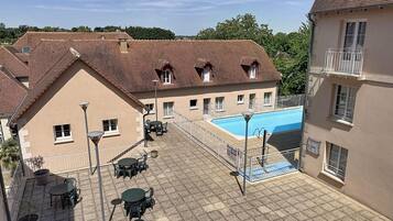 A courtyard with a swimming pool, outdoor seating, and a building with a tiled roof.