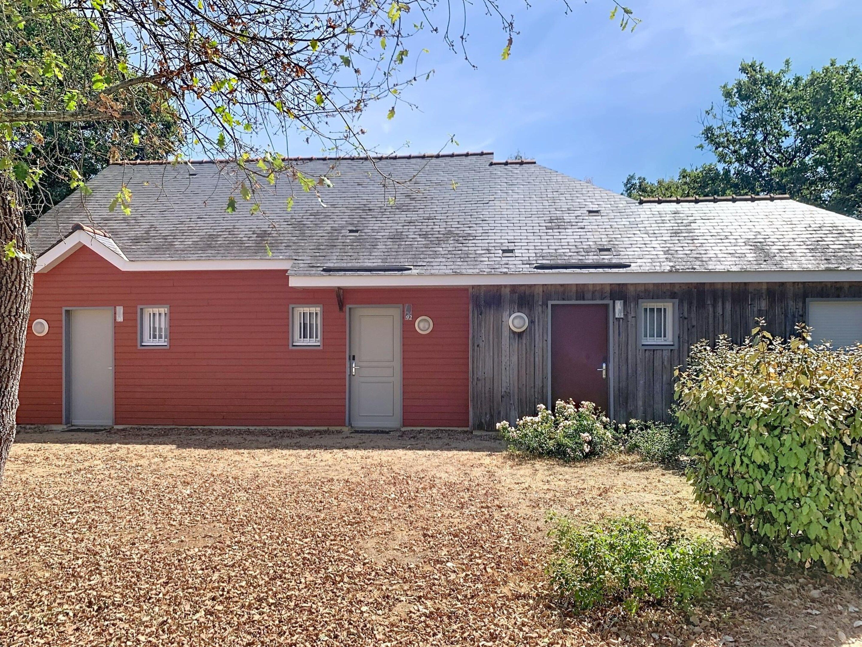 A red building with a grey roof, two doors, and a small window.
