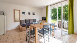 A modern living room with a sofa, a dining table with chairs, a television, and a sliding glass door leading to an outdoor area. - Spacious Duplex Cottage in Saumur (Saumur)