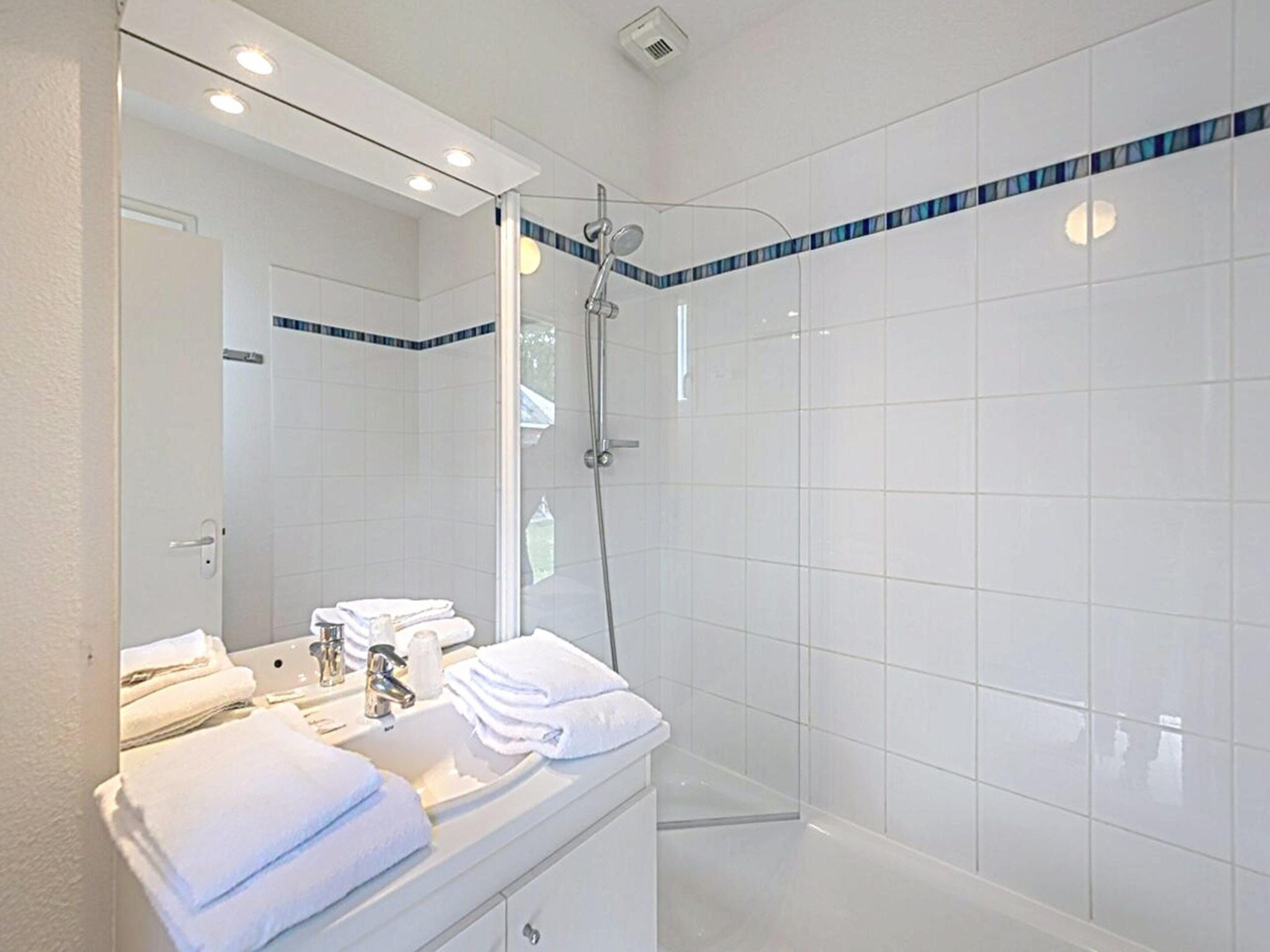 Een moderne badkamer met een glazen douchecabine, een wastafel met spiegel, en netjes opgevouwen handdoeken.