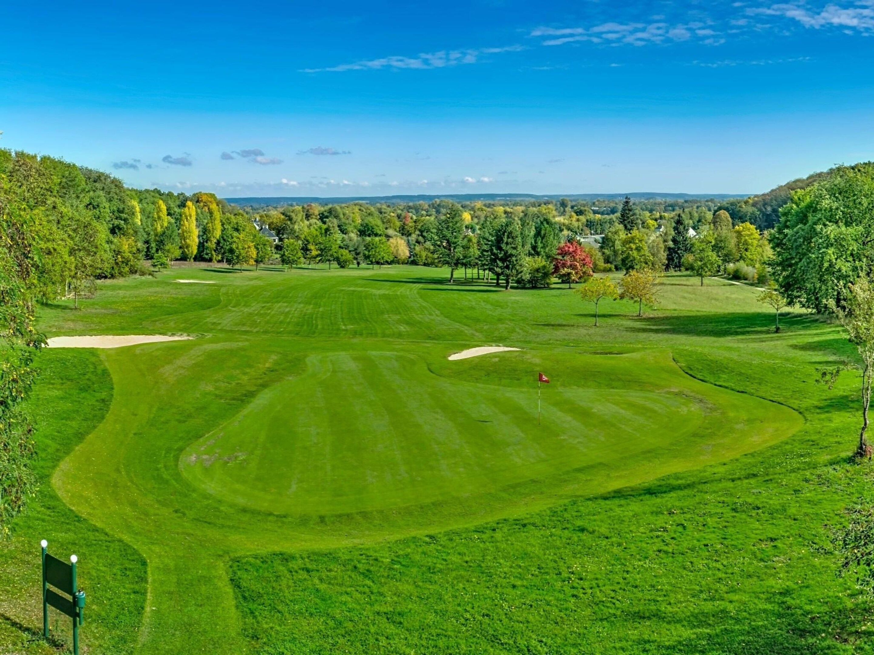 Un campo de golf con una bandera, bunkers de arena y cielo despejado.