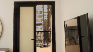 Una habitación con puerta de vidrio corrediza que da a un balcón exterior, un televisor de pantalla plana montado en la pared y piso de madera.