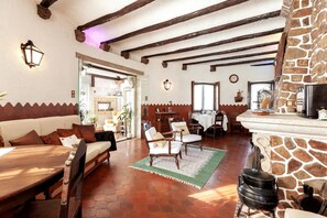 Tunnelmallinen, maalaishenkinen sisustus, jossa on esillä puupalkit, takka, ruokailutila ja kivielementeillä koristeltu keittiö.