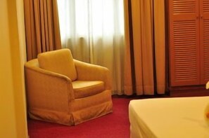 Une chambre d’hôtel avec un tapis rouge, un fauteuil jaune, un lit et une armoire en bois.