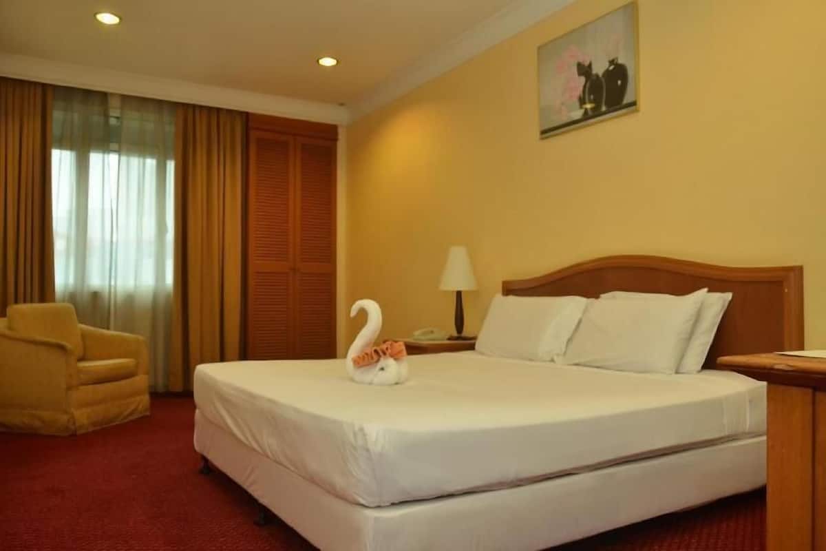 A hotel room with a bed, a chair, a lamp, and a painting on the wall.