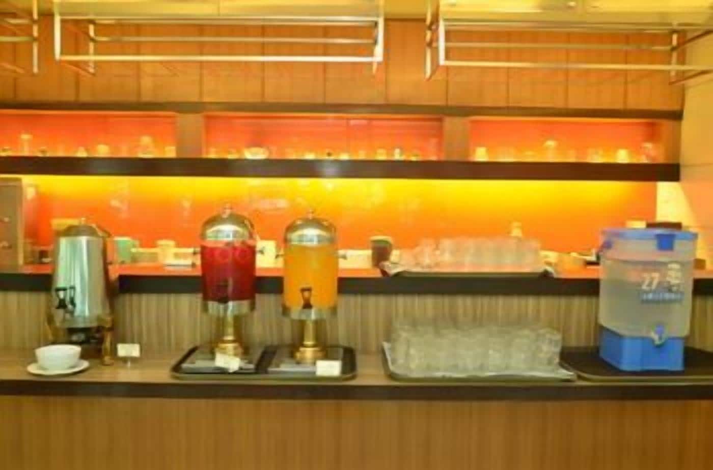 Un buffet de petit-déjeuner d’hôtel comprenant une machine à café, un distributeur de boissons chaudes, un distributeur de jus de fruits et un distributeur d’eau.