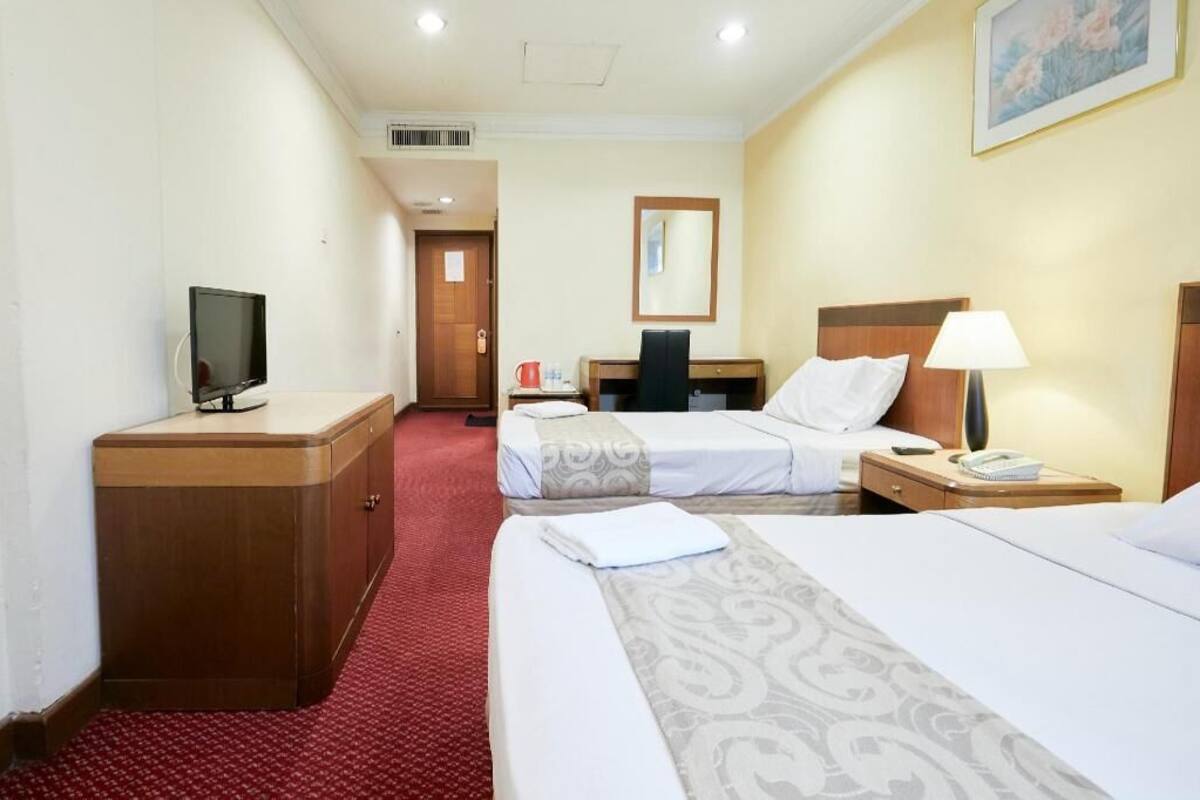 A hotel room with two beds, a desk, a TV, and a red carpet.