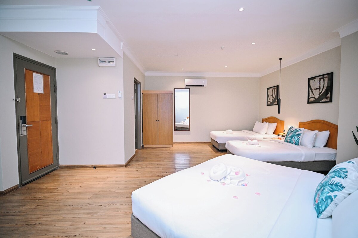 A hotel room with a wooden floor, two beds, a wardrobe, and a mirror.