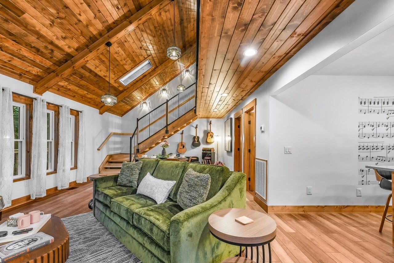 Un espacio habitable amplio con un sofá verde, piso de madera, una escalera y una pared decorada con notas musicales.