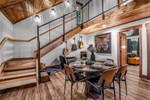 A modern interior with a wooden staircase, dining area with chairs and a table, and guitars on the wall.