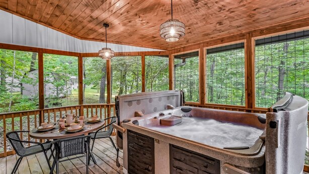 A wooden deck with a hot tub, a table with chairs, and a view of a forest. - Dolly's Harmony Haven 3 Bedroom Cabin (Sevierville)