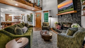 A spacious living area with a high ceiling, a fireplace, and a large painting of a sunset. - Dolly's Harmony Haven 3 Bedroom Cabin (Sevierville)