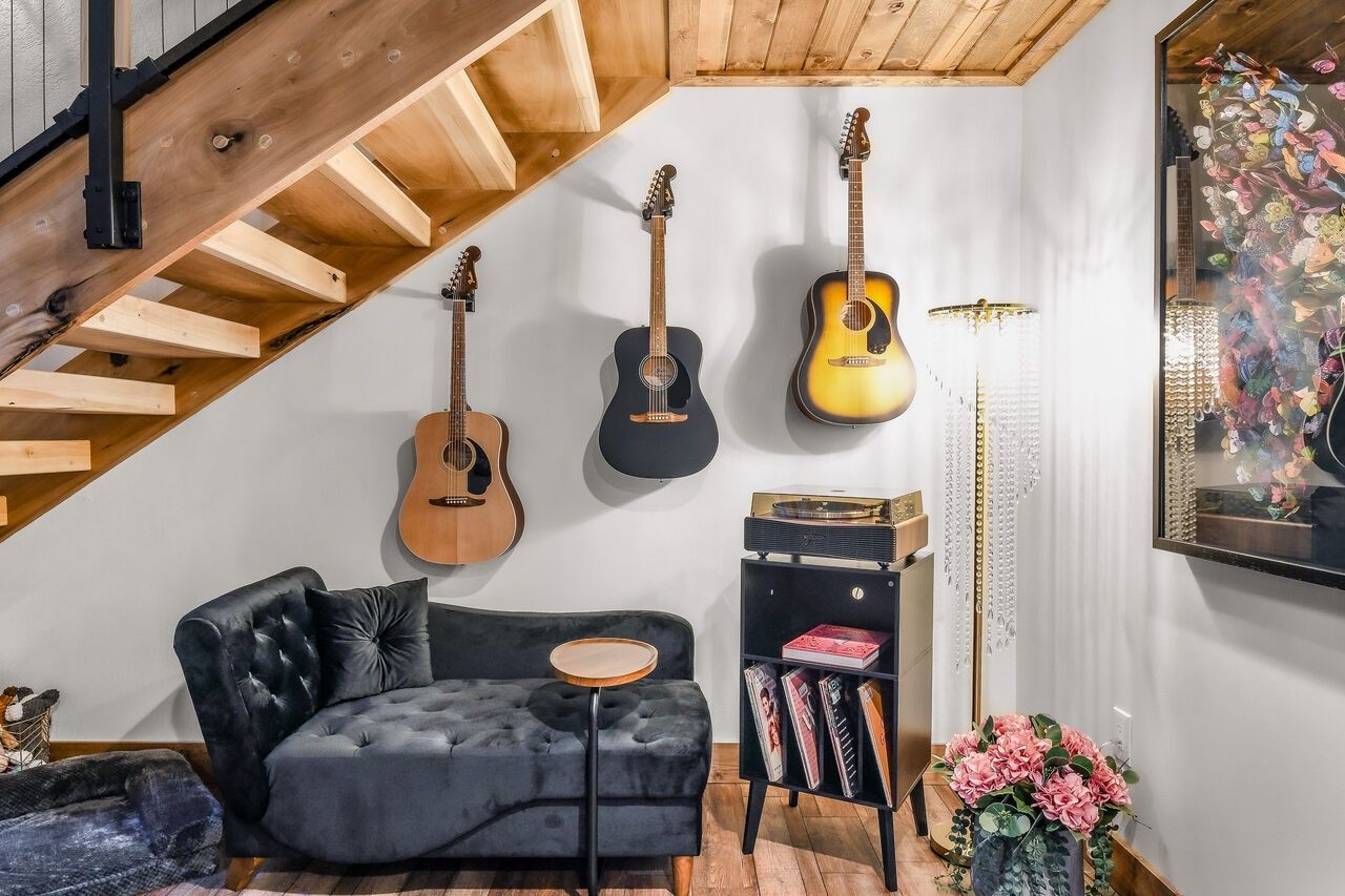 Ein Wohnzimmer mit einem schwarzen Sofa, einer Holztreppe und drei Gitarren an der Wand.