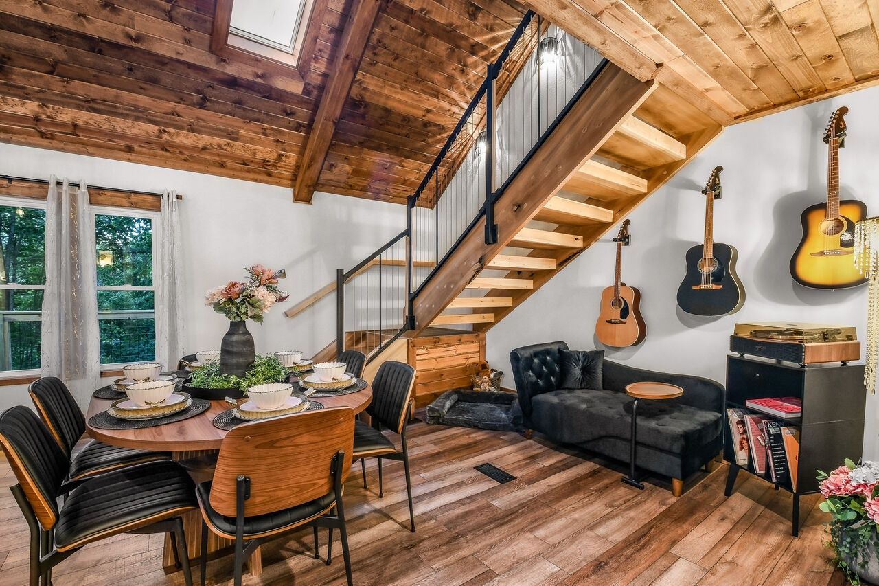 Un comedor con mesa y sillas de madera, una escalera con barandilla de madera y un sofá negro.