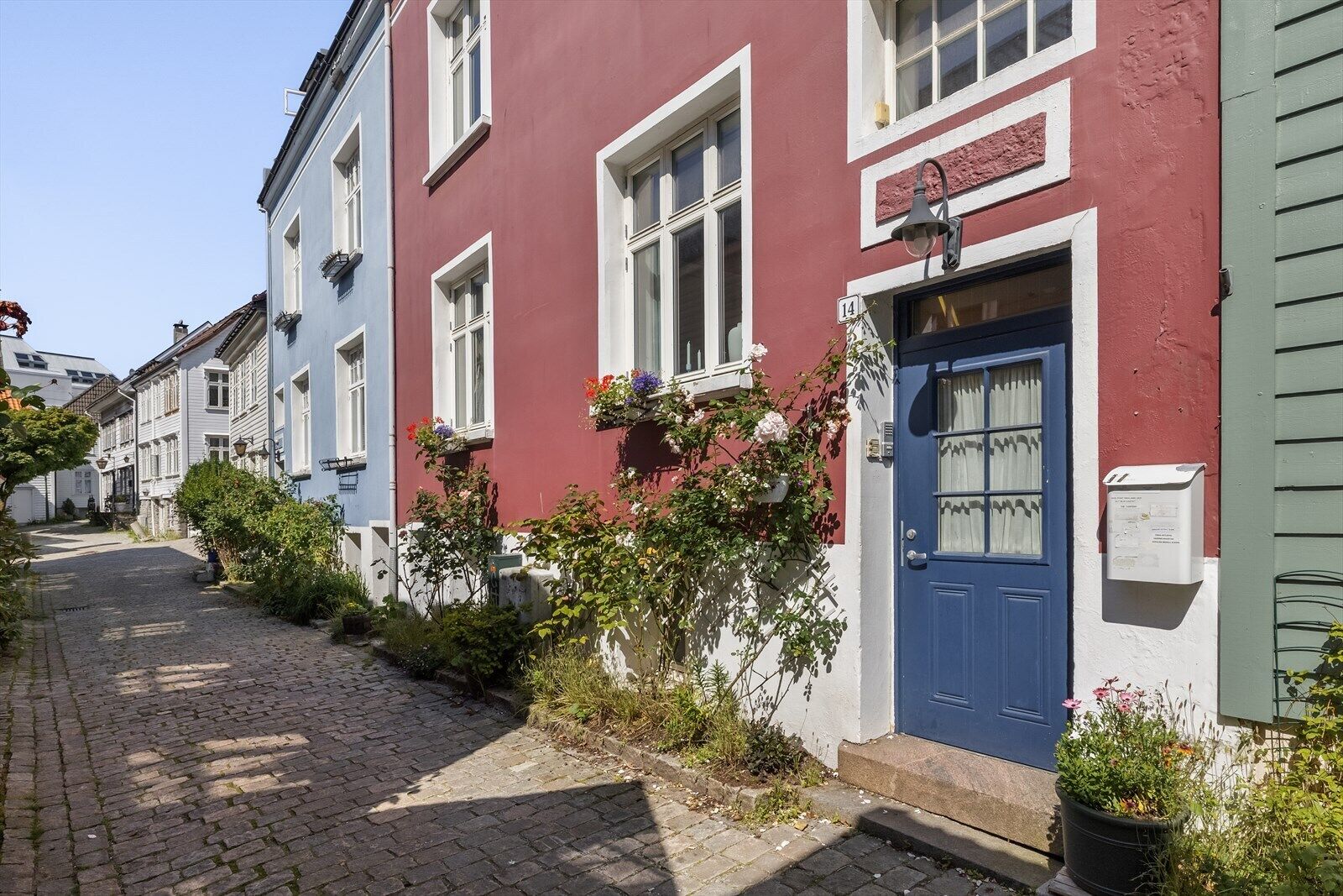 A narrow cobblestone street lined with colorful buildings, a blue door, and flower boxes on the windows.