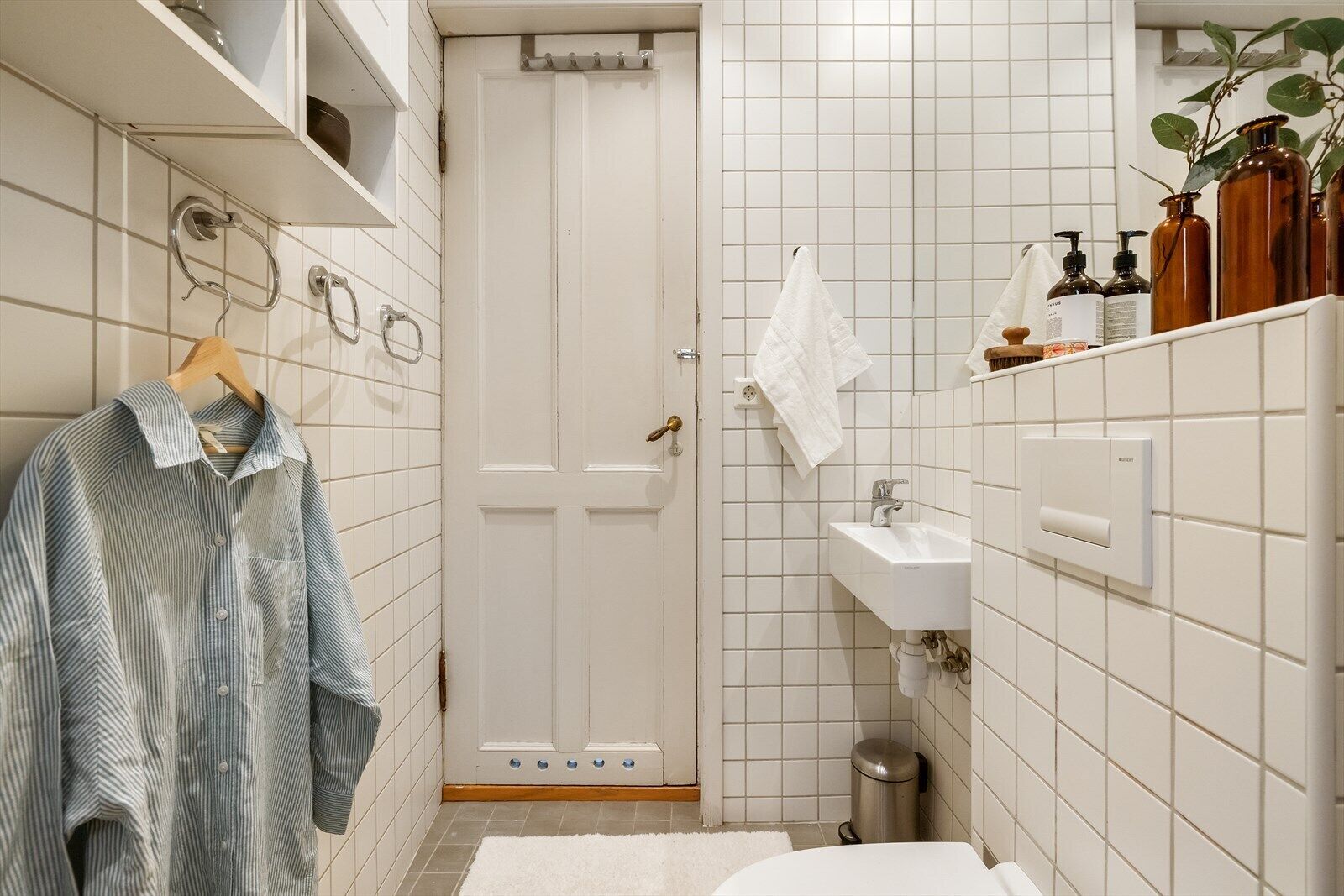 Un baño con pared de azulejos blancos, un lavamanos, un inodoro y un perchero para toallas.