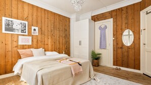Ein Schlafzimmer mit Holzwandverkleidung, einem Bett mit weißer Bettwäsche, einem aufgehängten Kleid und einem Spiegel an der Wand.