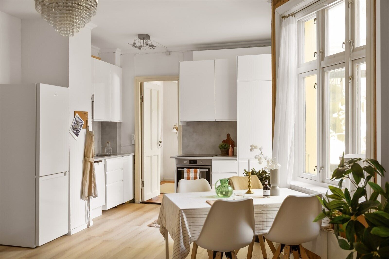 Una cocina moderna con armarios blancos, una mesa de comedor con sillas y un amplio ventanal con cortinas.