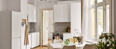 Una cocina moderna con armarios blancos, una mesa de comedor con sillas y un amplio ventanal con cortinas.