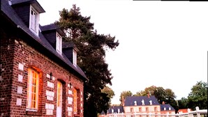 Een bakstenen gebouw met een witte hek, grote ramen en een boom ervoor.