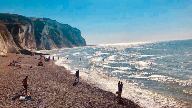 Een strand met mensen, kliffen en de oceaan.