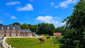 Een landelijk landschap met een witte omheining, een grasveld en een groot gebouw met een rood dak.