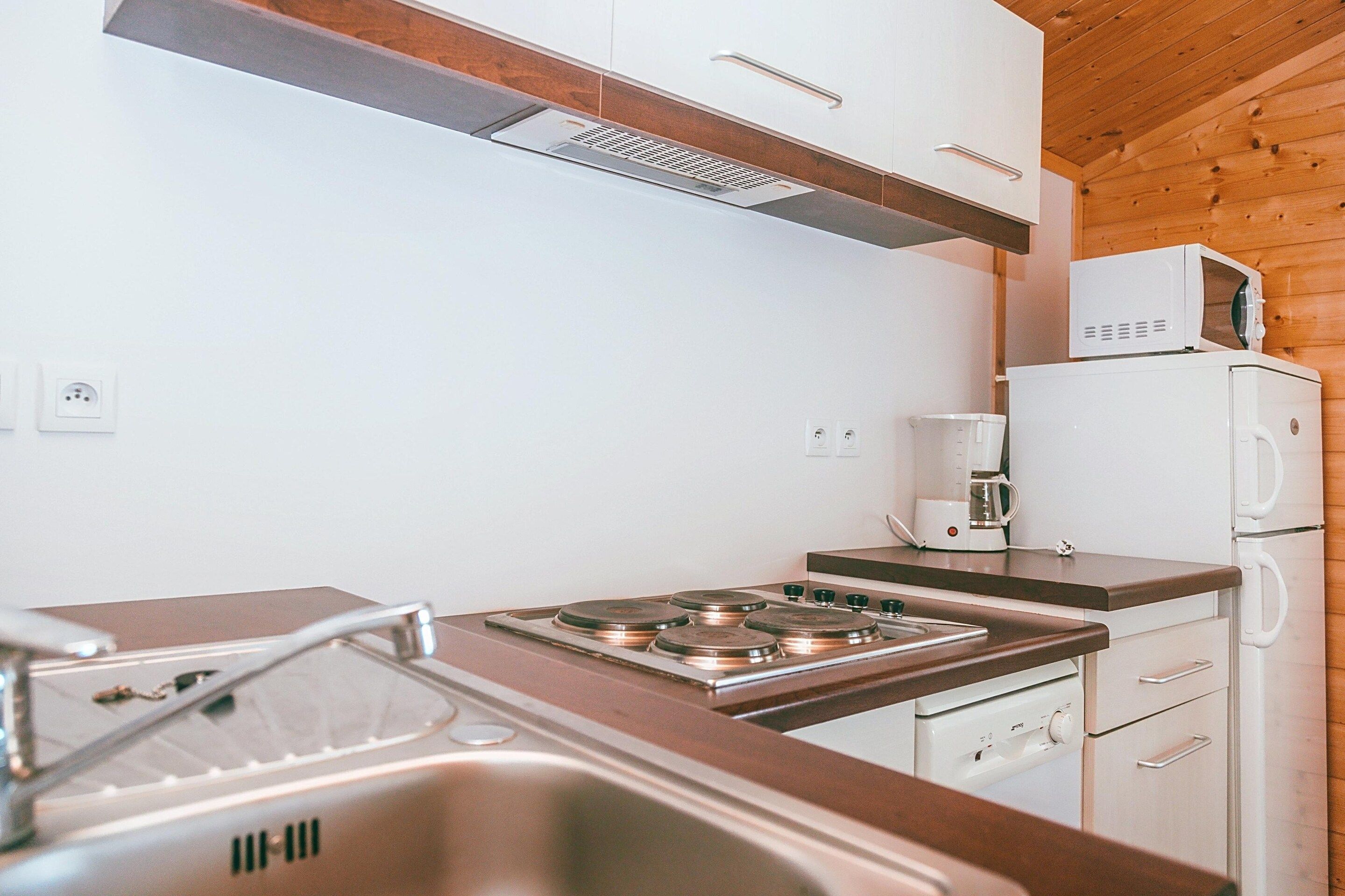 A compact kitchen with a stove, sink, and a microwave on a wooden cabinet.