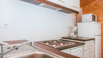 A compact kitchen with a stove, sink, and a microwave on a wooden cabinet.