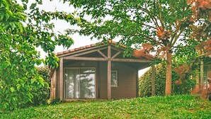 Un piccolo chalet di legno con tetto spiovente, immerso nel verde e circondato da alberi.