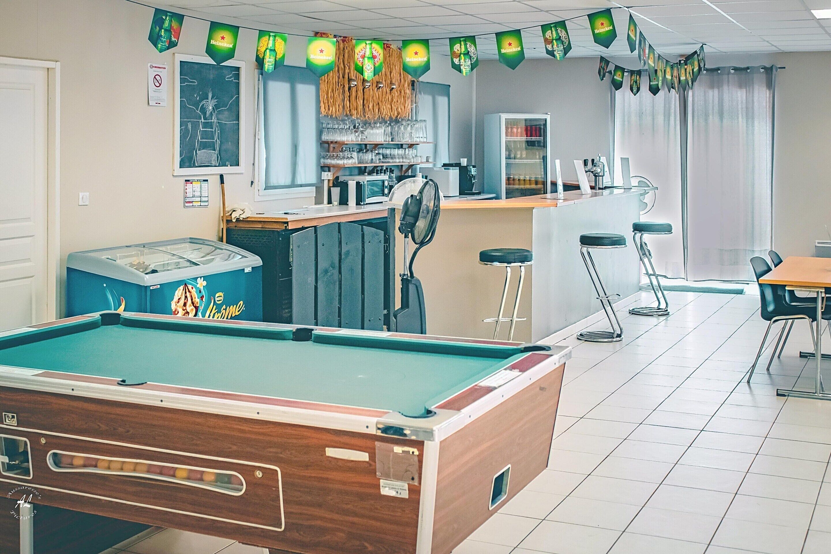 Mesa de billar, zona de bar y asientos en una sala con suelo de baldosas.