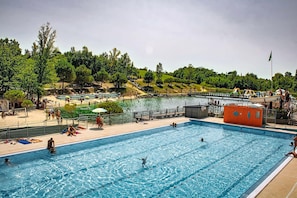 Ein Schwimmbecken mit klarem Wasser, umgeben von einer Liegefläche mit Bänken und Sonnenschirmen.