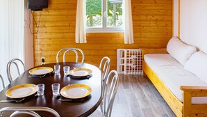 Interno di una baita di legno con un tavolo da pranzo apparecchiato per quattro persone, un divano e una televisione a parete.