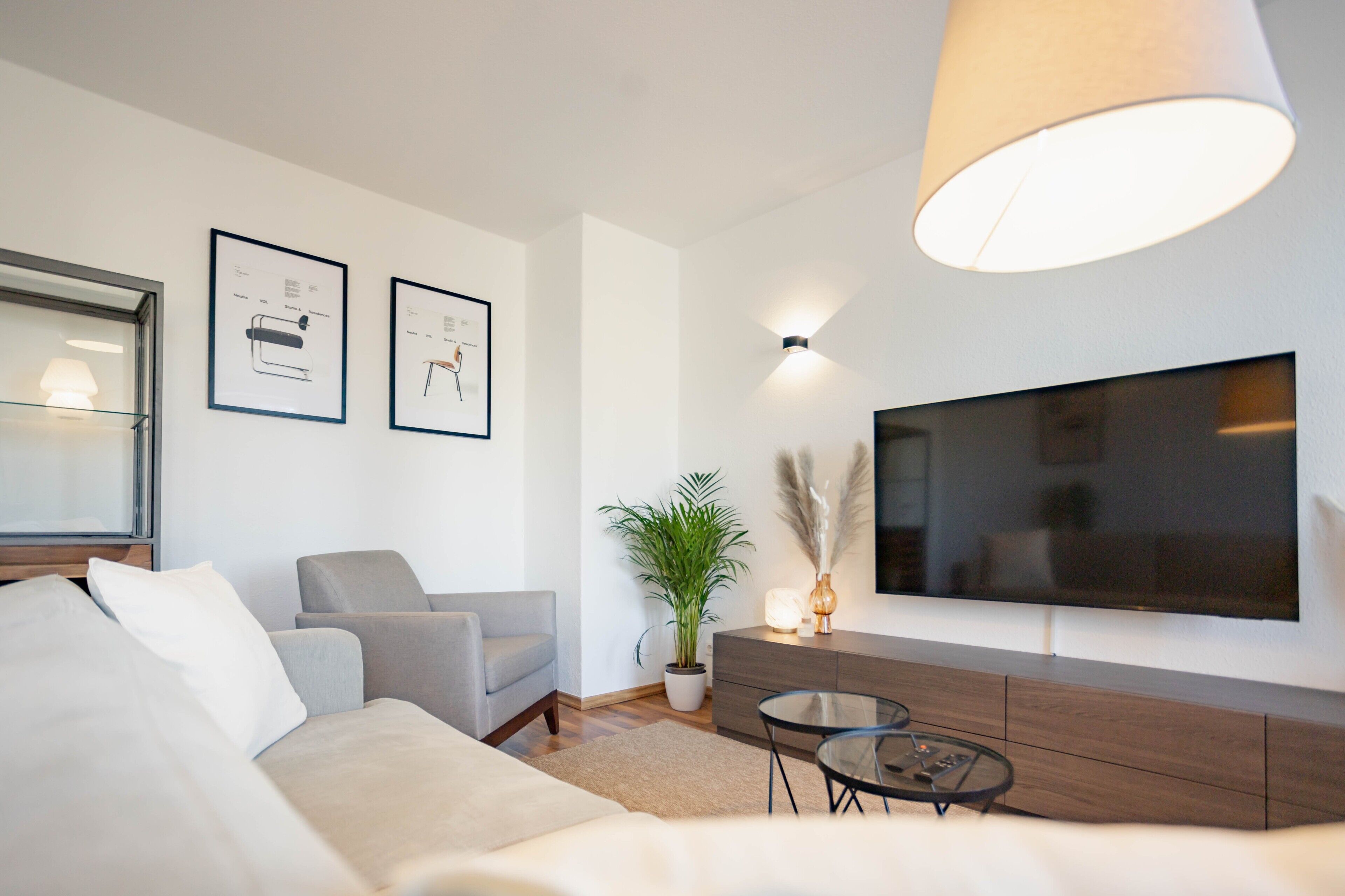 Un salon moderne avec un canapé, un fauteuil, une télévision et une plante en pot.
