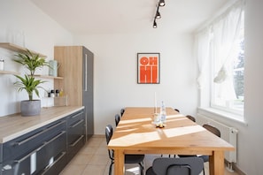 A modern kitchen with a wooden table, chairs, and a potted plant.