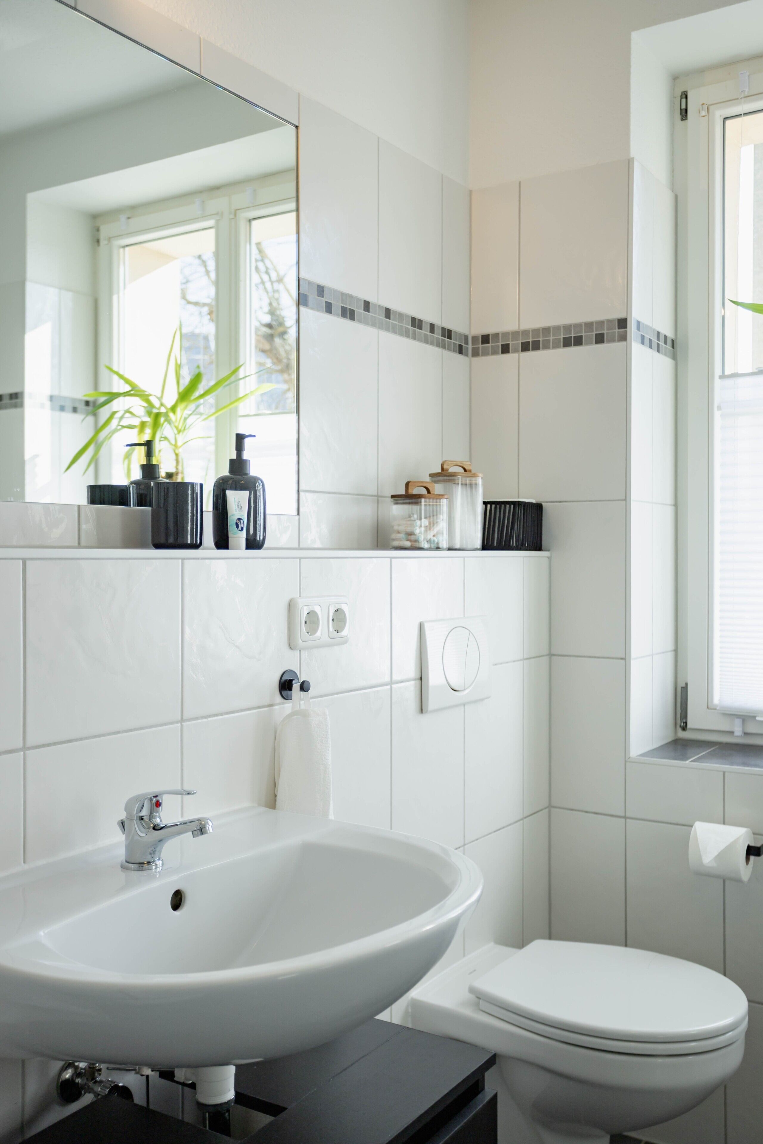 A bathroom with a white sink, a toilet, a mirror, and a window with blinds.