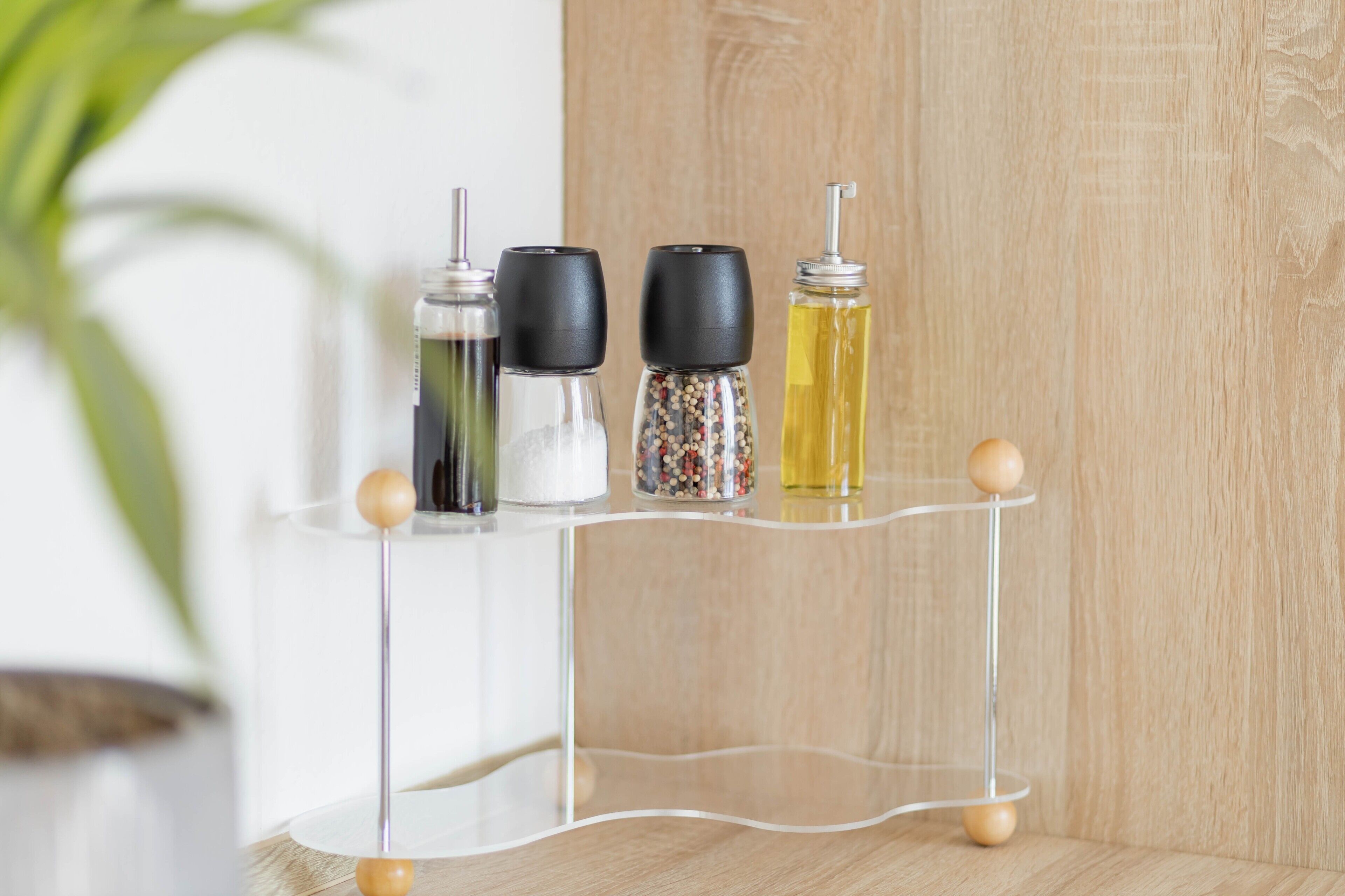 A clear, modern kitchen shelf with four spice containers and a clear glass bottle.