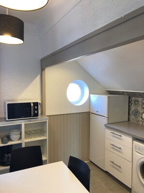 A compact kitchen with a microwave, a sink, and a washing machine. There is a dining table with chairs and a small window. - 55 m² two-room apartment in Villejuif, 6 minutes from the metro (Villejuif)