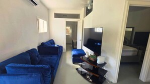 Un salon avec un canapé bleu, un téléviseur à écran plat posé sur un meuble et un ventilateur de plafond.