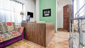 A reception desk with a 'HOTEL' sign, a wooden reception desk, a purple sofa, a monitor, and a green wall. - Hotel O Rajendra Nagar Hingna Road (Nagpur)