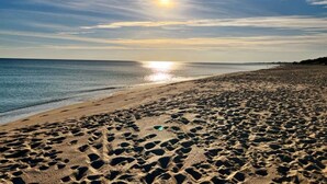 A beach with footprints in the sand and the sun setting over the water.