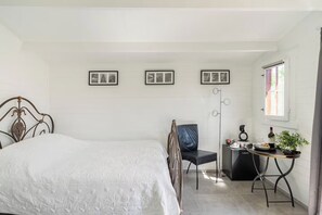 A bedroom with a bed, a chair, a small table with a plant, and three framed pictures on the wall.
