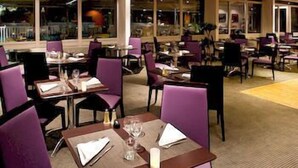 Een restaurant met paarse stoelen, tafels gedekt met wijnglazen en een vloerkleed.
